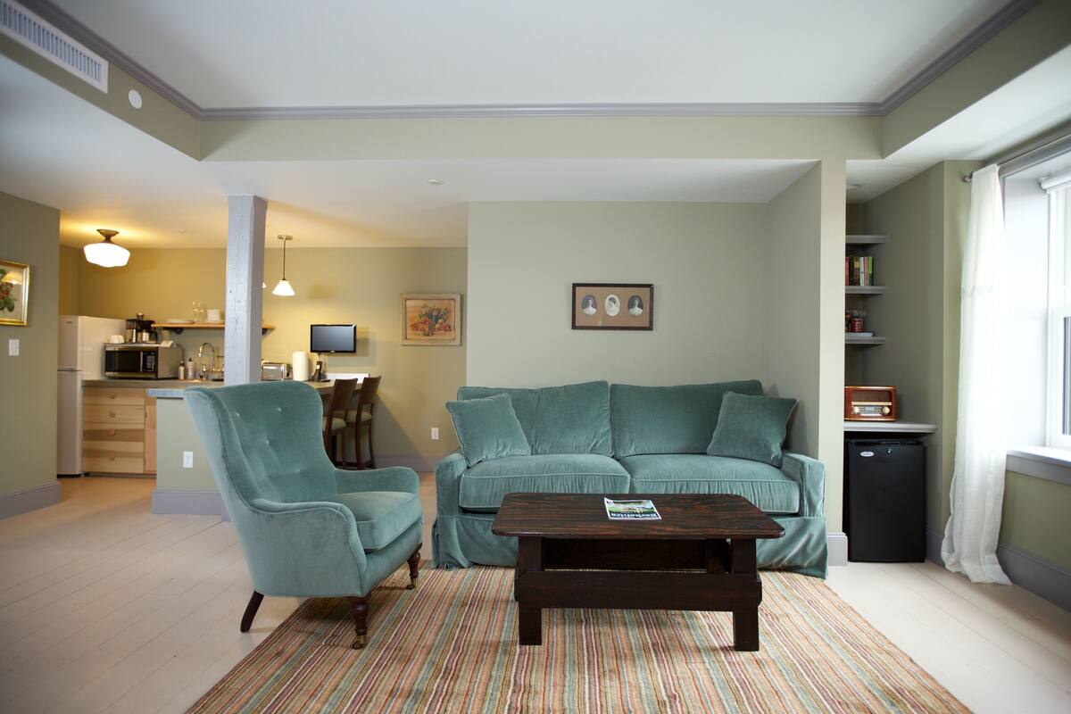 A living room with a teal sofa, a wooden coffee table, and a striped rug.