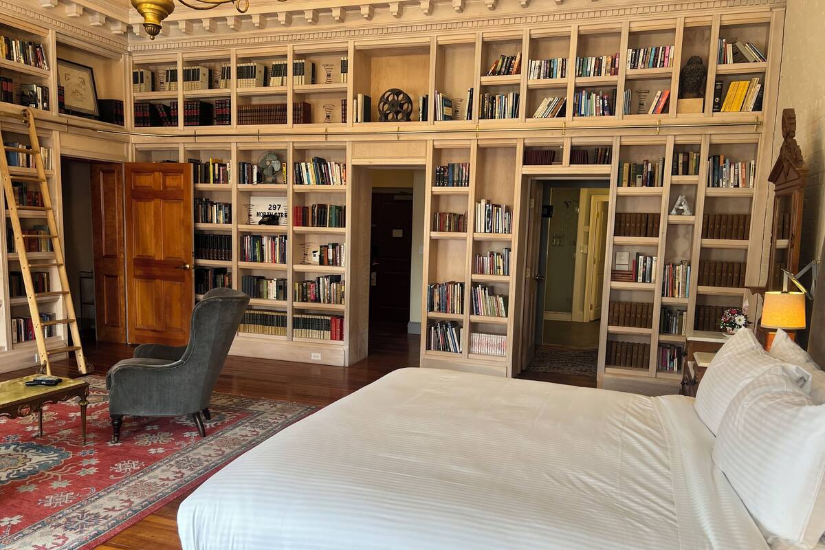 A spacious bedroom with a large bed, a wooden ladder, and a bookshelf filled with books.
