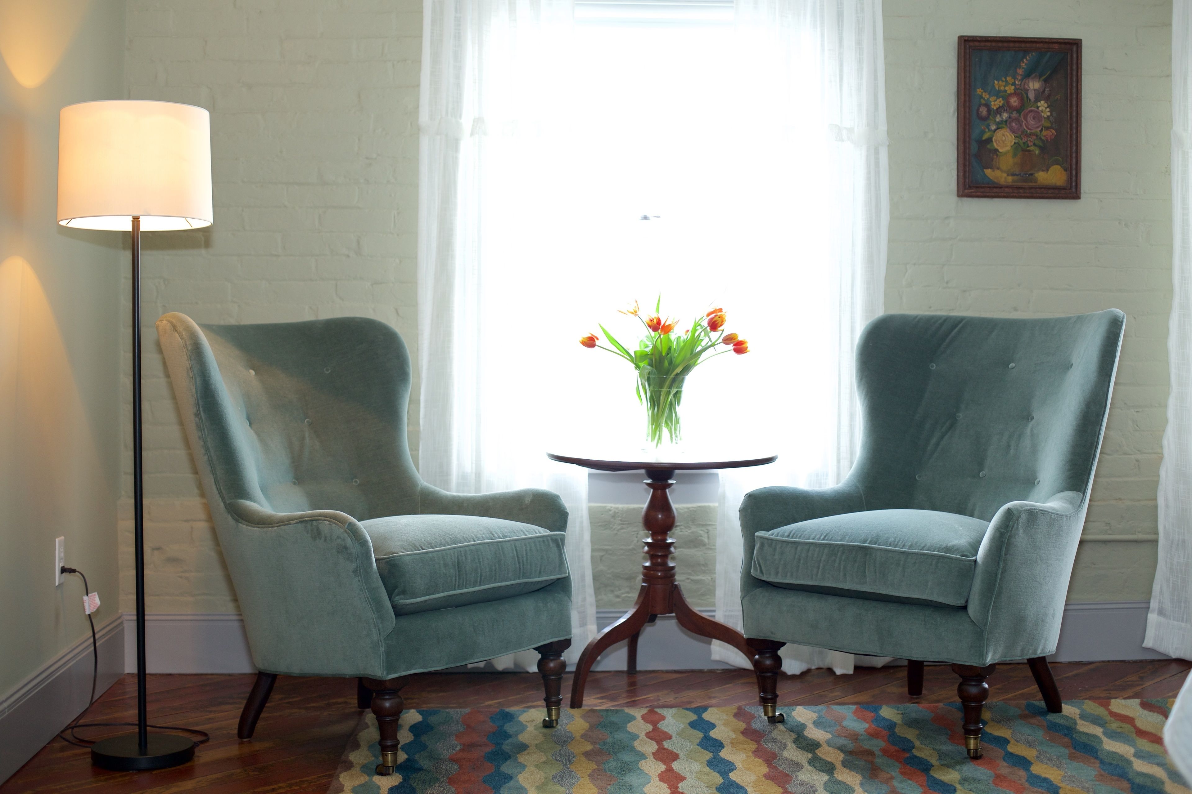 Two armchairs facing each other with a small round table between them, a floor lamp to the left, and a colorful rug on the floor.