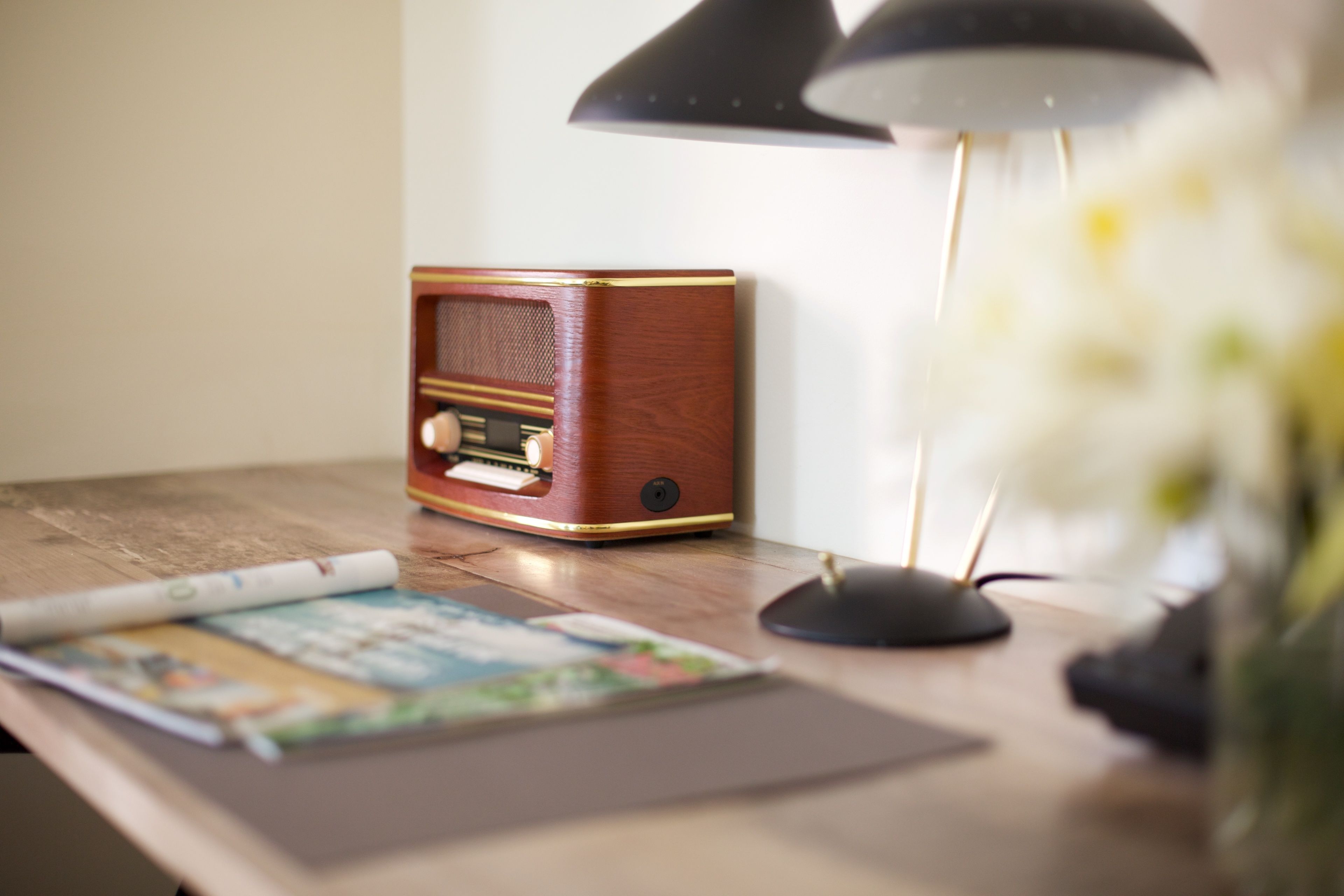 Un escritorio de madera con una radio antigua, una lámpara y una revista enrollada.