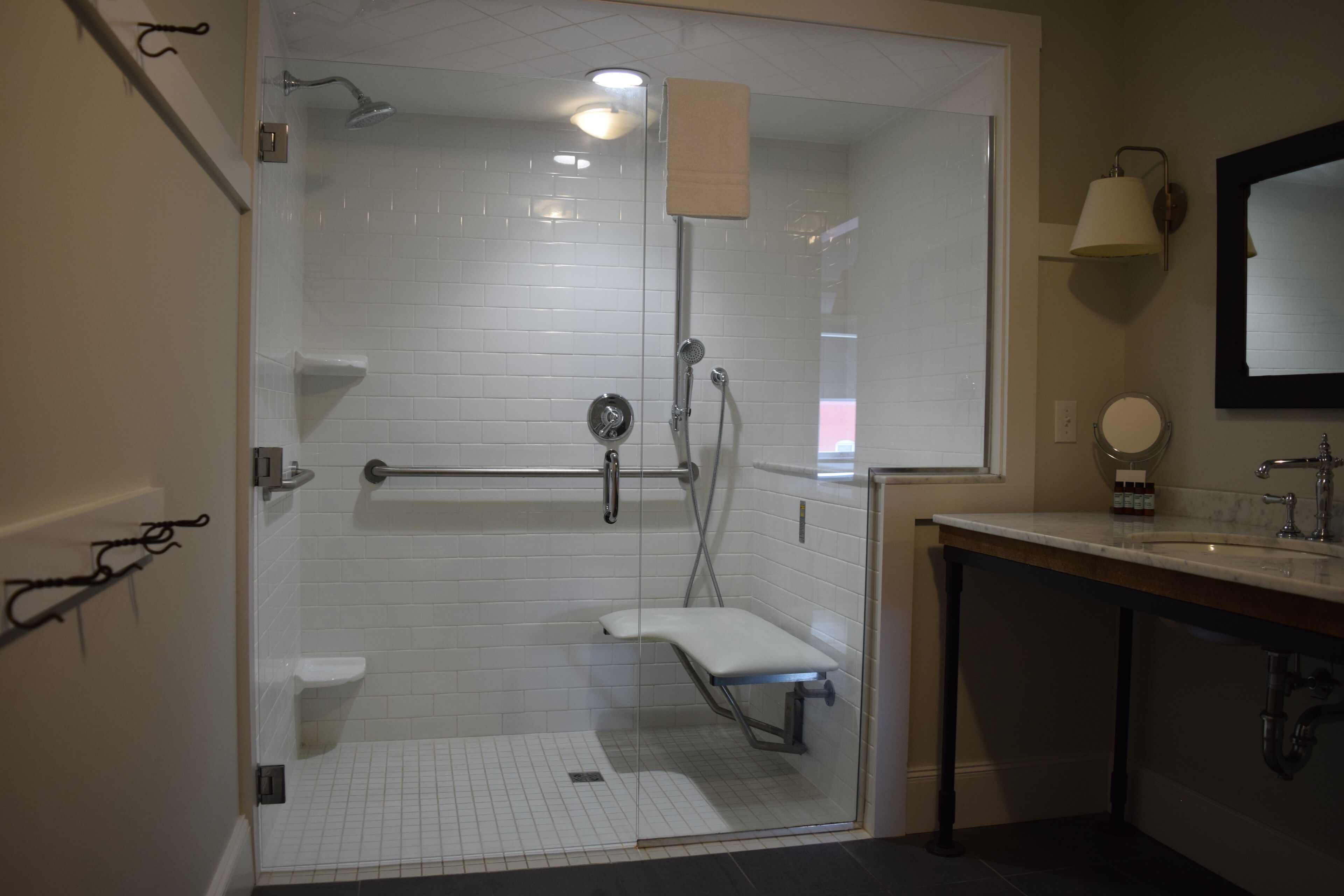 Un bagno moderno con doccia vetro-murata, pavimento piastrellato in bianco, divisorio in vetro, water bianco e mobile lavabo con specchio.