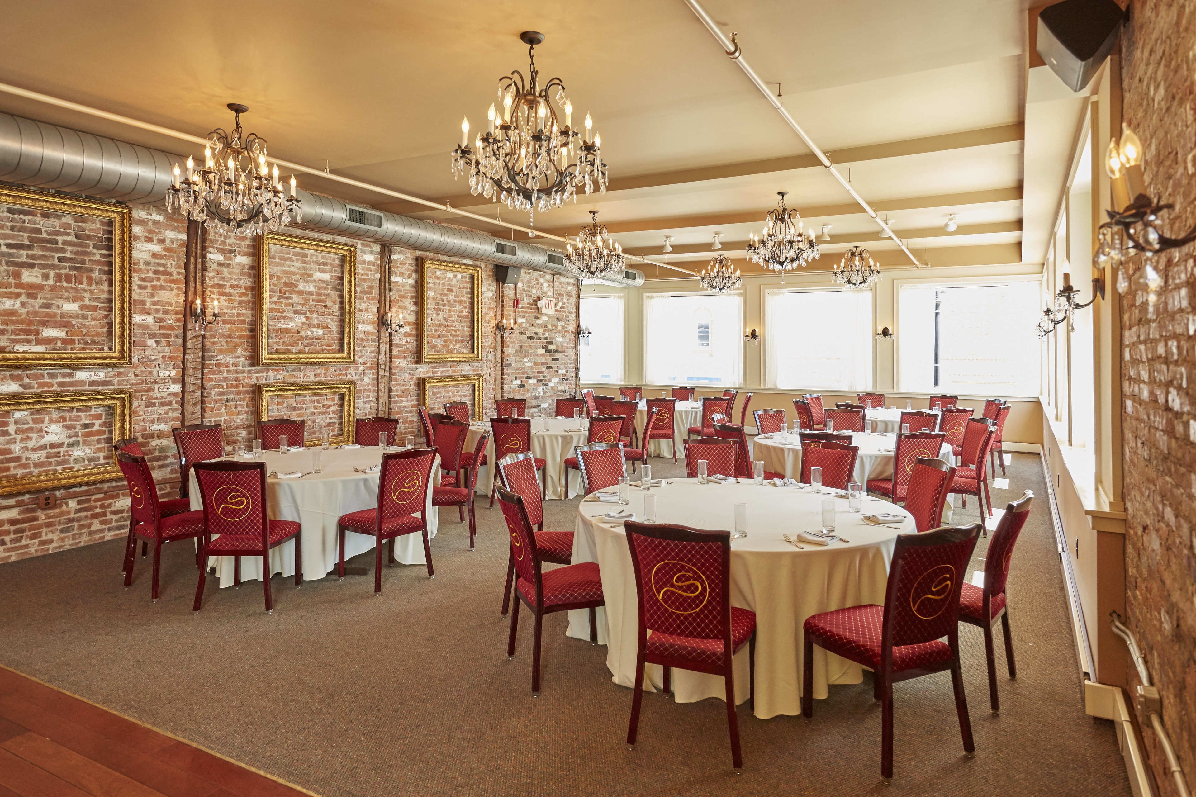 A conference room with round tables and red chairs, large windows, and chandeliers.