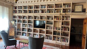 A library with bookshelves, a television, and two armchairs. - Hotel On North (Pittsfield)