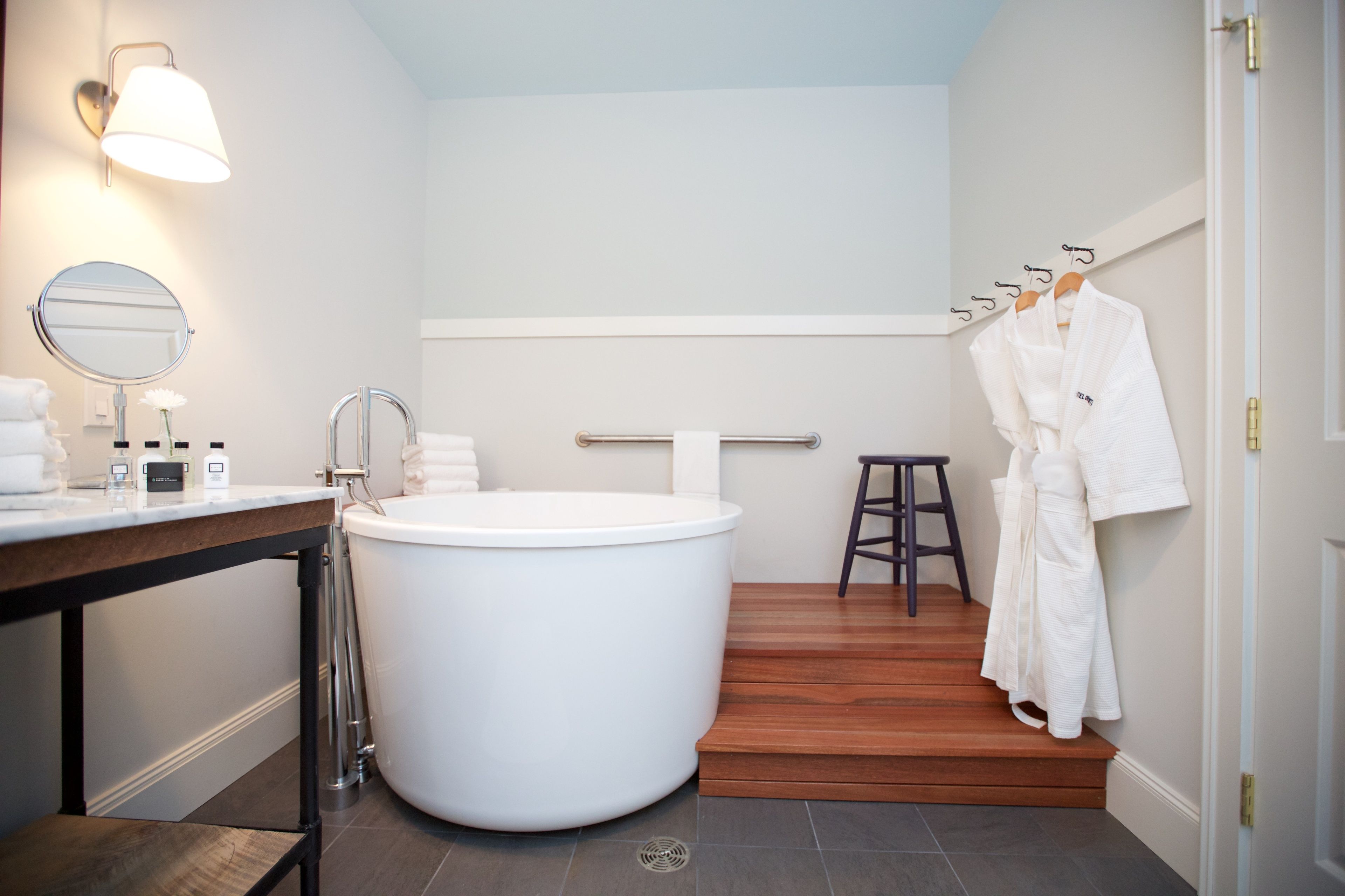 Ein modernes Badezimmer mit einer großen Badewanne, einem hölzernen Hocker und einem Handtuchhalter mit Bademänteln.