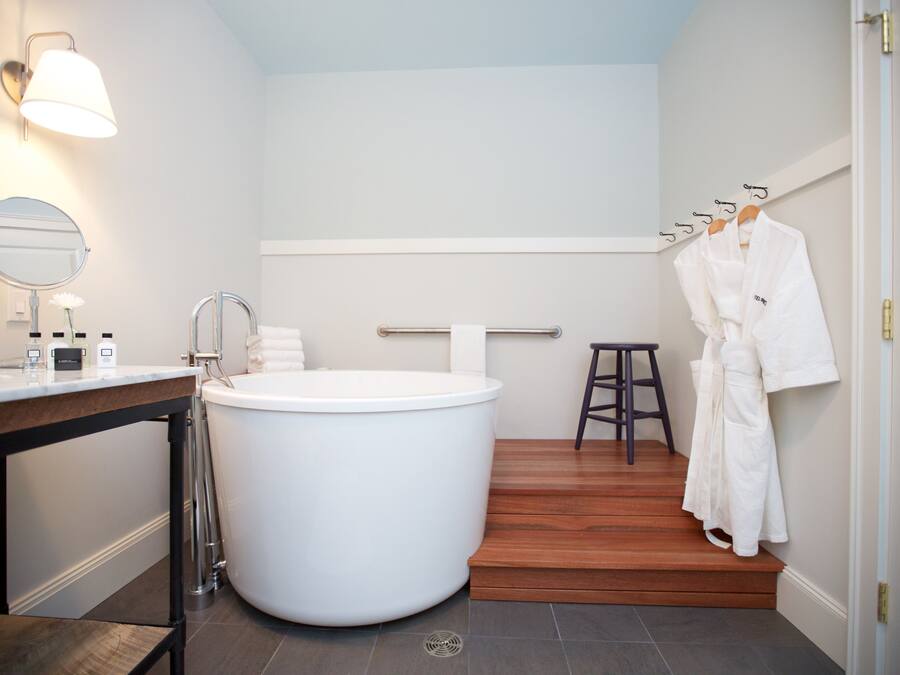 Ein modernes Badezimmer mit einer großen Badewanne, einem hölzernen Hocker und einem Handtuchhalter mit Bademänteln.