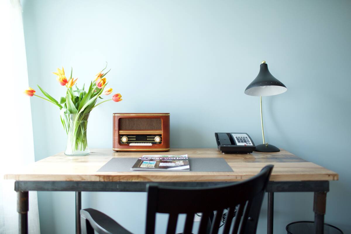 A wooden table with a radio, a telephone, and a vase of flowers.