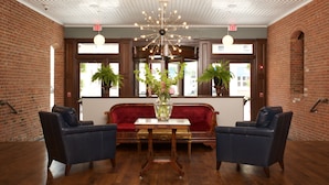 A lobby with a red sofa, two armchairs, a wooden table with a vase, brick walls, and an ornate ceiling. - Hotel On North (Pittsfield)