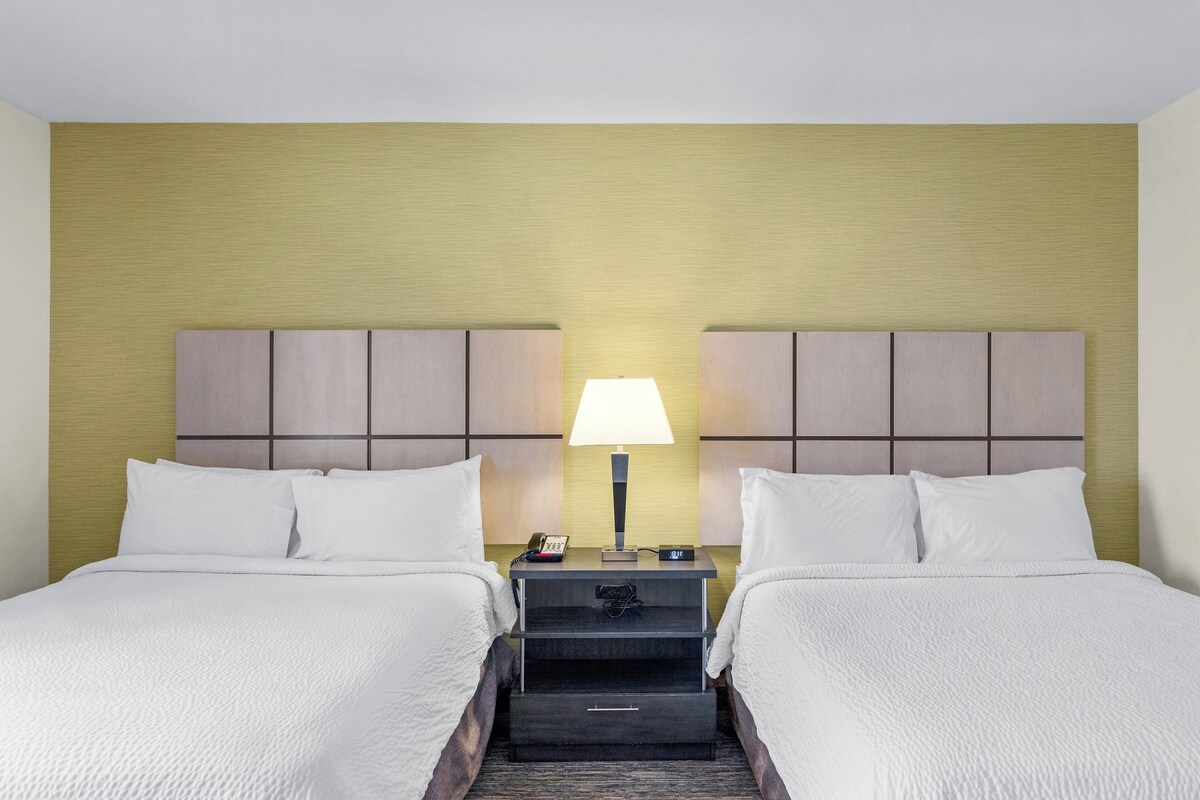 A hotel room with two beds, a nightstand with a lamp, and a small drawer.