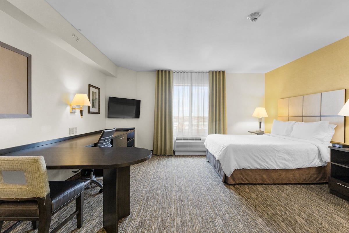 Habitación de hotel con cama, escritorio, silla, televisor y ventana con cortinas.