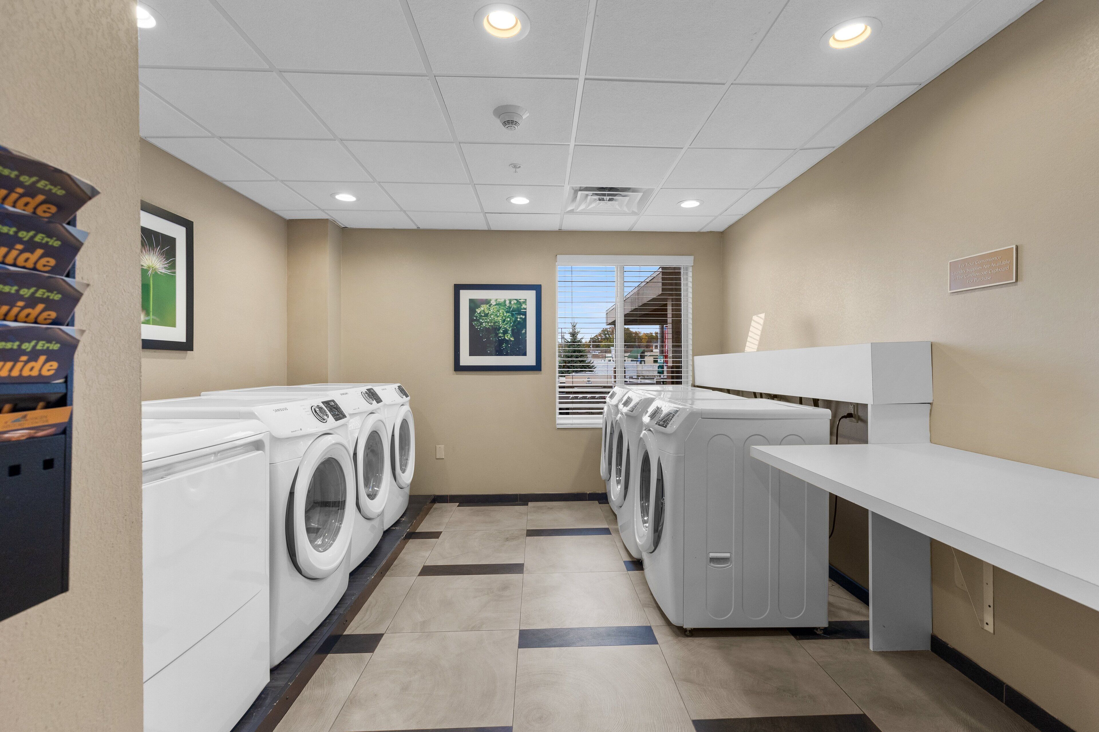 A laundry room with multiple washing machines, a drying rack, and a wall-mounted rack with folded towels.