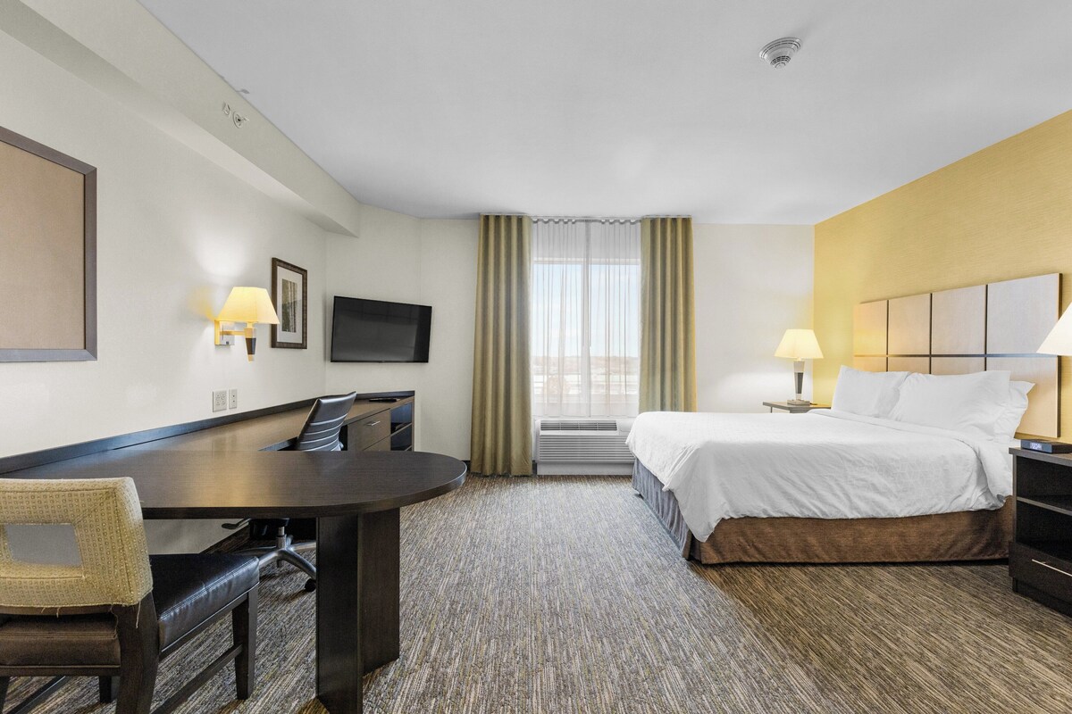 A hotel room with a bed, a desk, a chair, a TV, and a window with curtains.