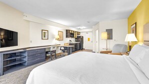 Una habitación de hotel con una cama grande, un escritorio con silla, televisión y kitchenette.