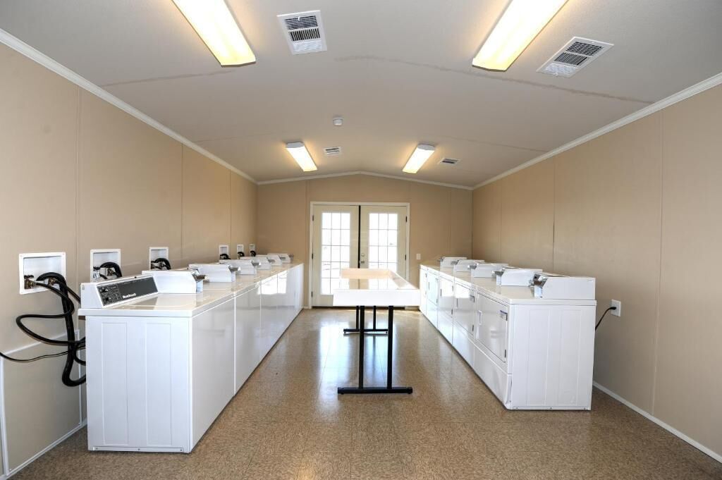 A laundry facility with multiple washing machines and dryers, a central table, and fluorescent lighting.