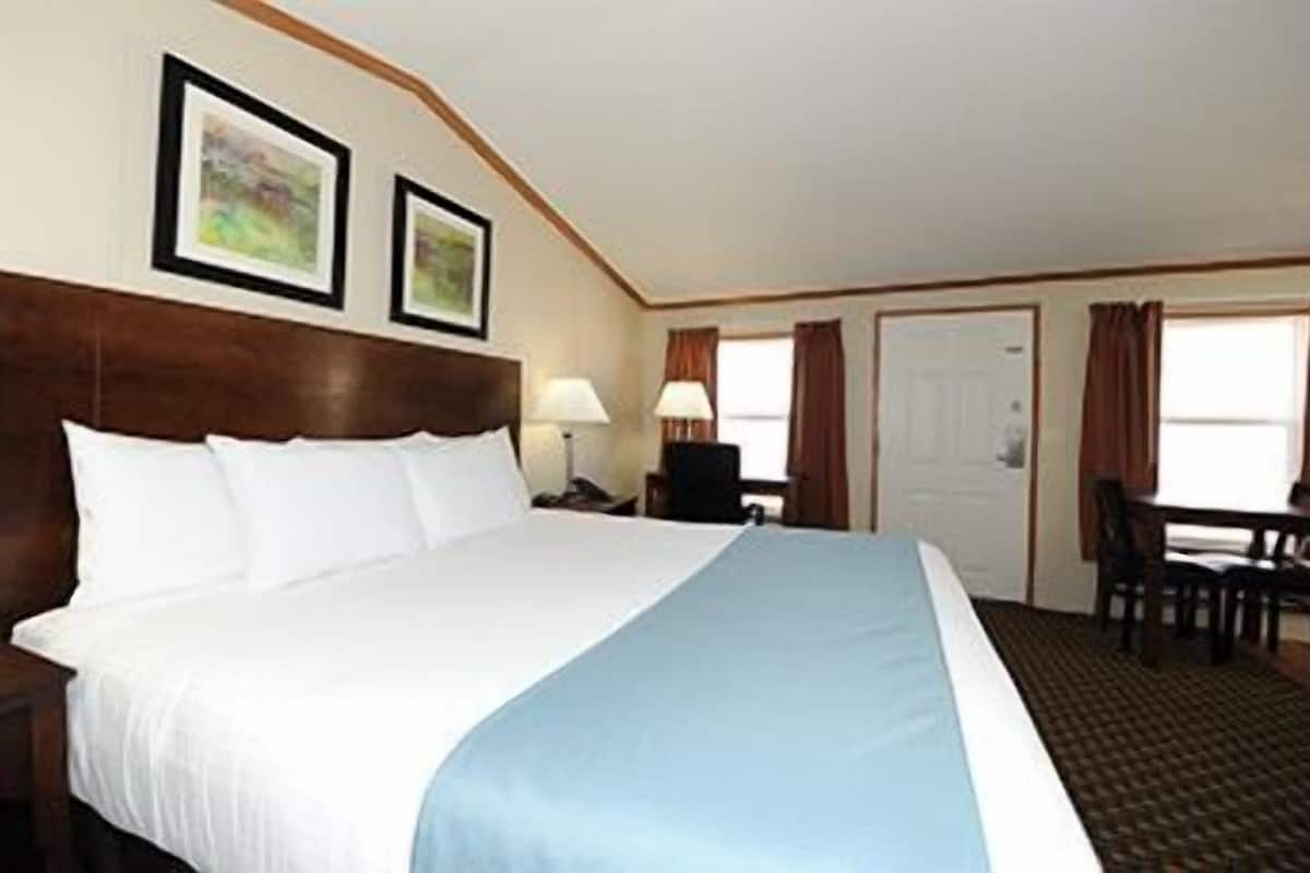 A hotel room with a large bed, a desk, and two framed pictures on the wall.