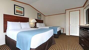 A hotel room with two beds, a dresser, a television, and a patterned carpet.