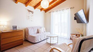 A modern living room with a wooden ceiling, a sofa, a chair, a TV mounted on the wall, and a small table.