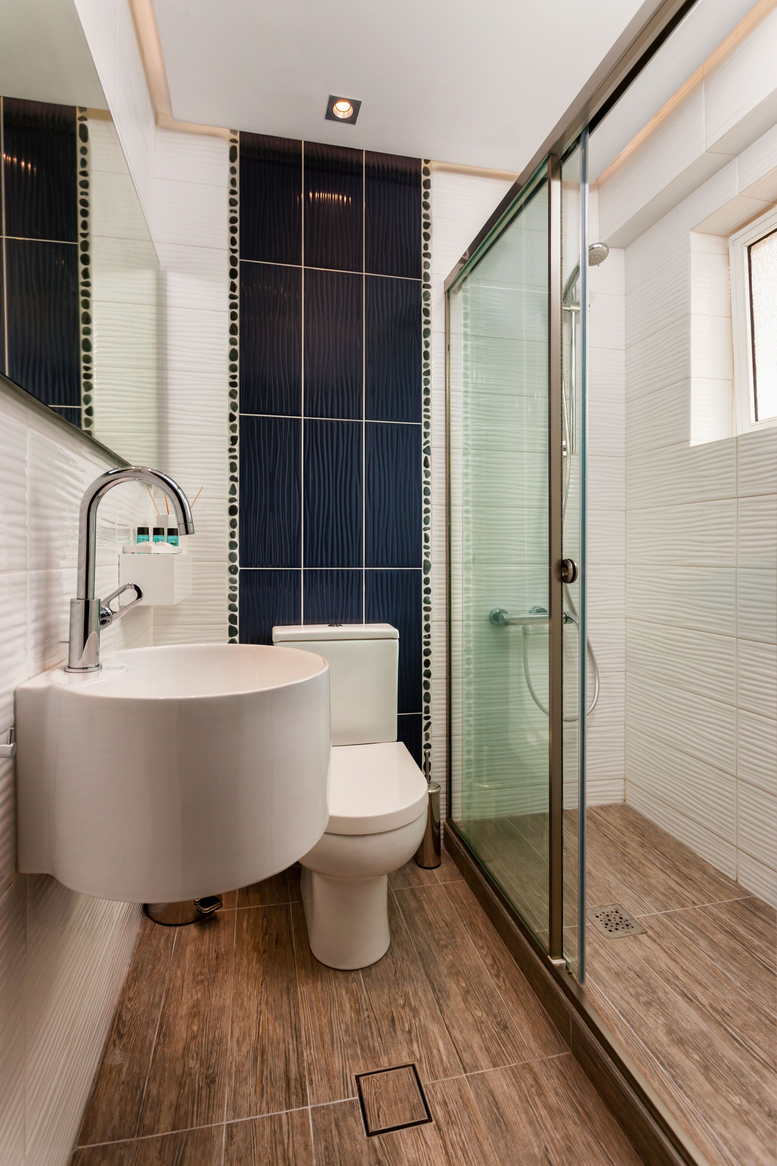 A modern bathroom with a round sink, toilet, and a glass shower enclosure.