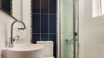 A modern bathroom with a round sink, toilet, and a glass shower enclosure.