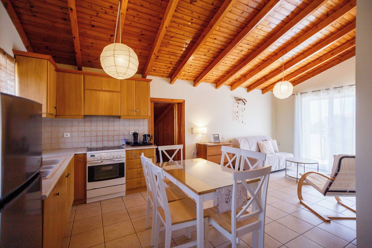 A kitchen with wooden cabinets, a dining table with chairs, a sofa, and a rocking chair.
