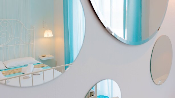 Un dormitorio moderno con cama, mesita de noche, lámpara y tres espejos.