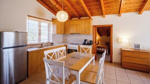Una cocina con armarios de madera, un refrigerador de acero inoxidable, una mesa de comedor con sillas y un techo de madera.