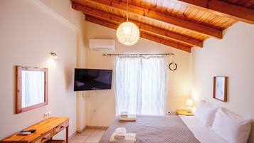 Ein Schlafzimmer mit Holzboden, einem Bett mit weißen Leinentüchern, einem Schreibtisch mit Stuhl, einem an der Wand montierten Flachbildfernseher und einem Fenster mit Vorhängen.