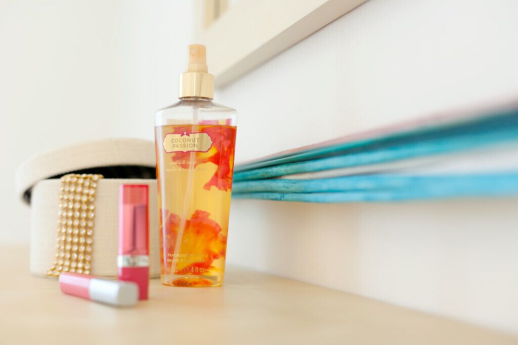 Een fles kokos-passie douchegel, een roze lippenbalsem en een haarborstel op een plank.