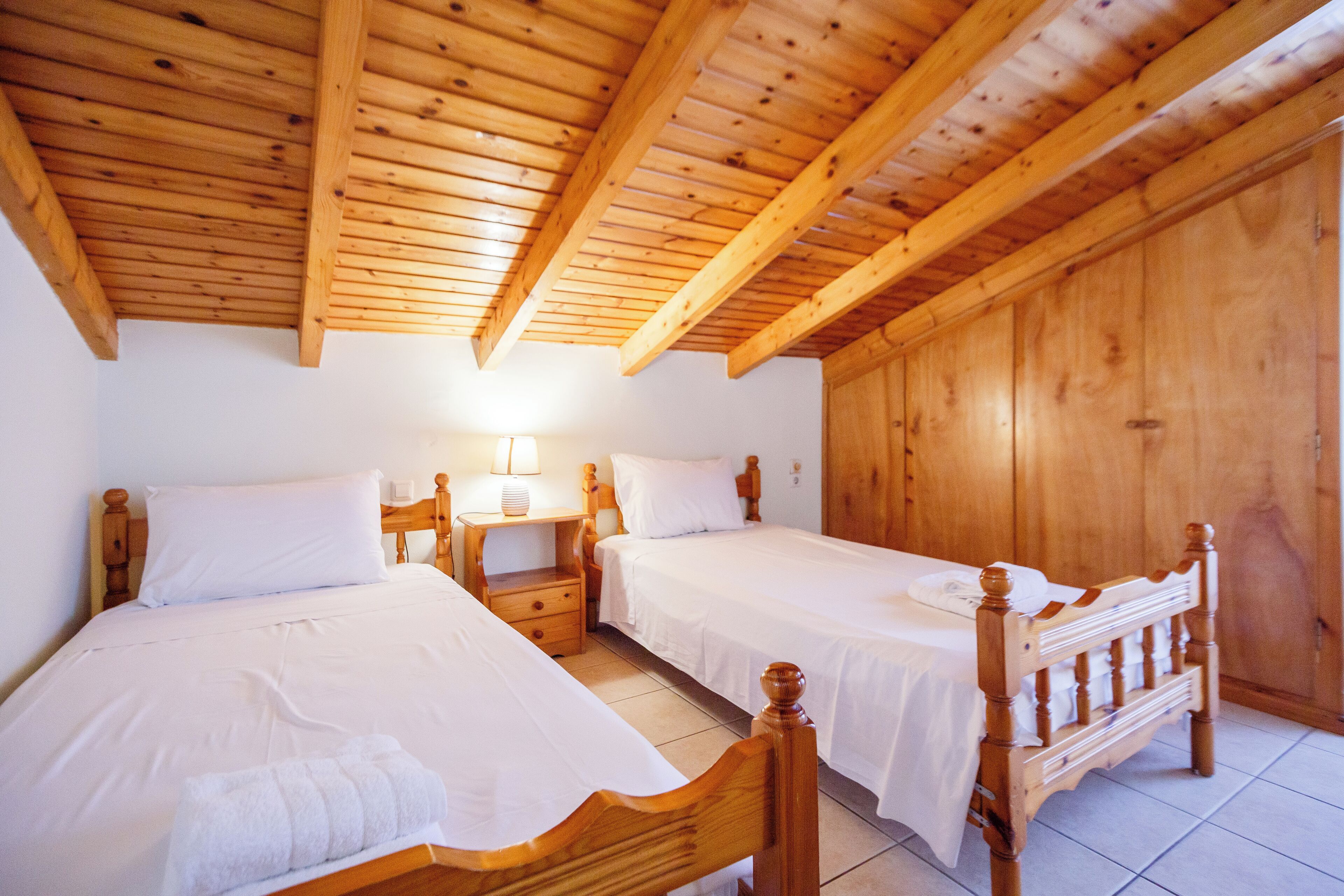 Una habitación de madera con dos camas, una mesita de noche y una lámpara.