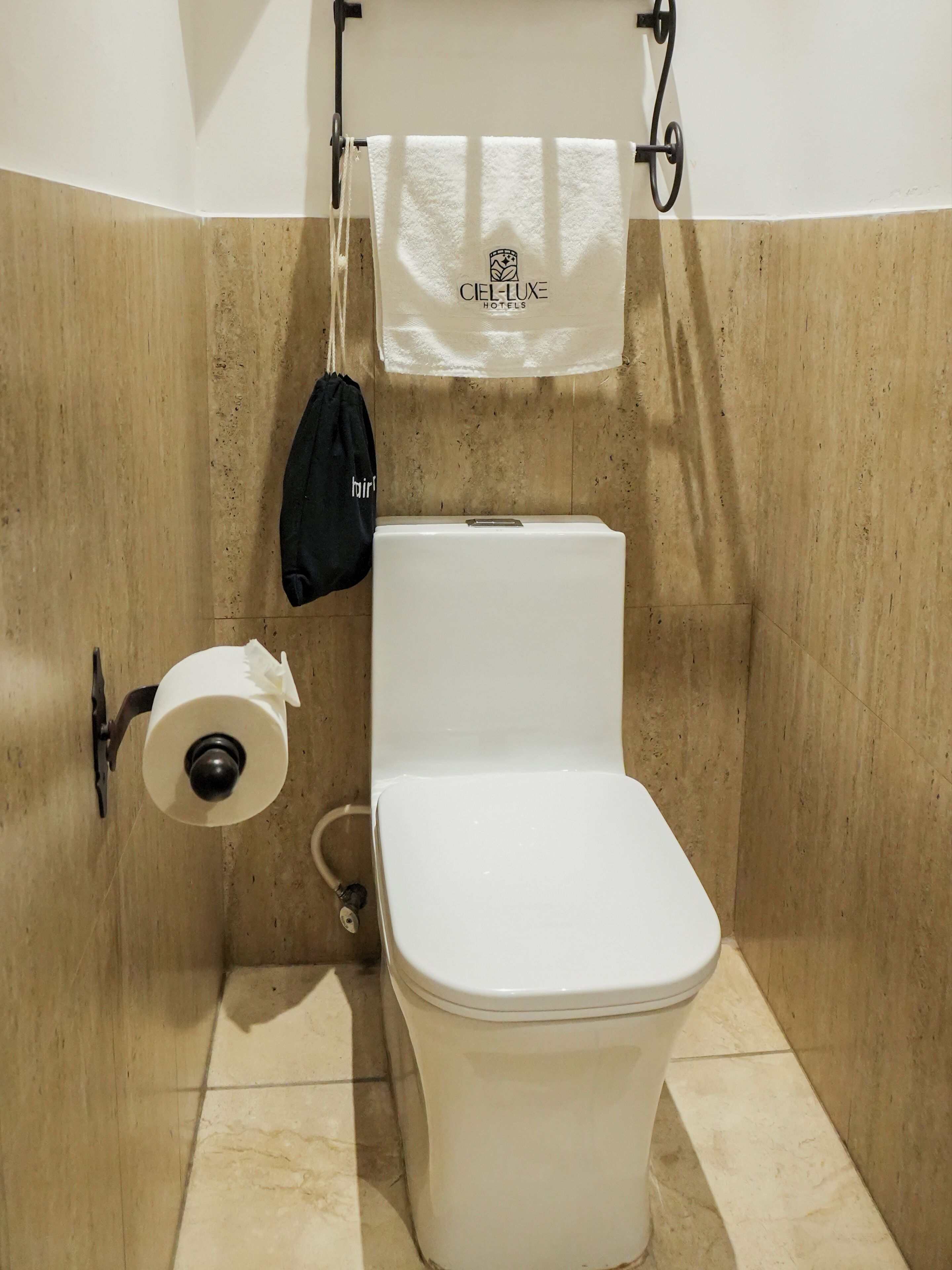 A bathroom with a toilet, a towel hanging on a rack, and a bag on the wall.