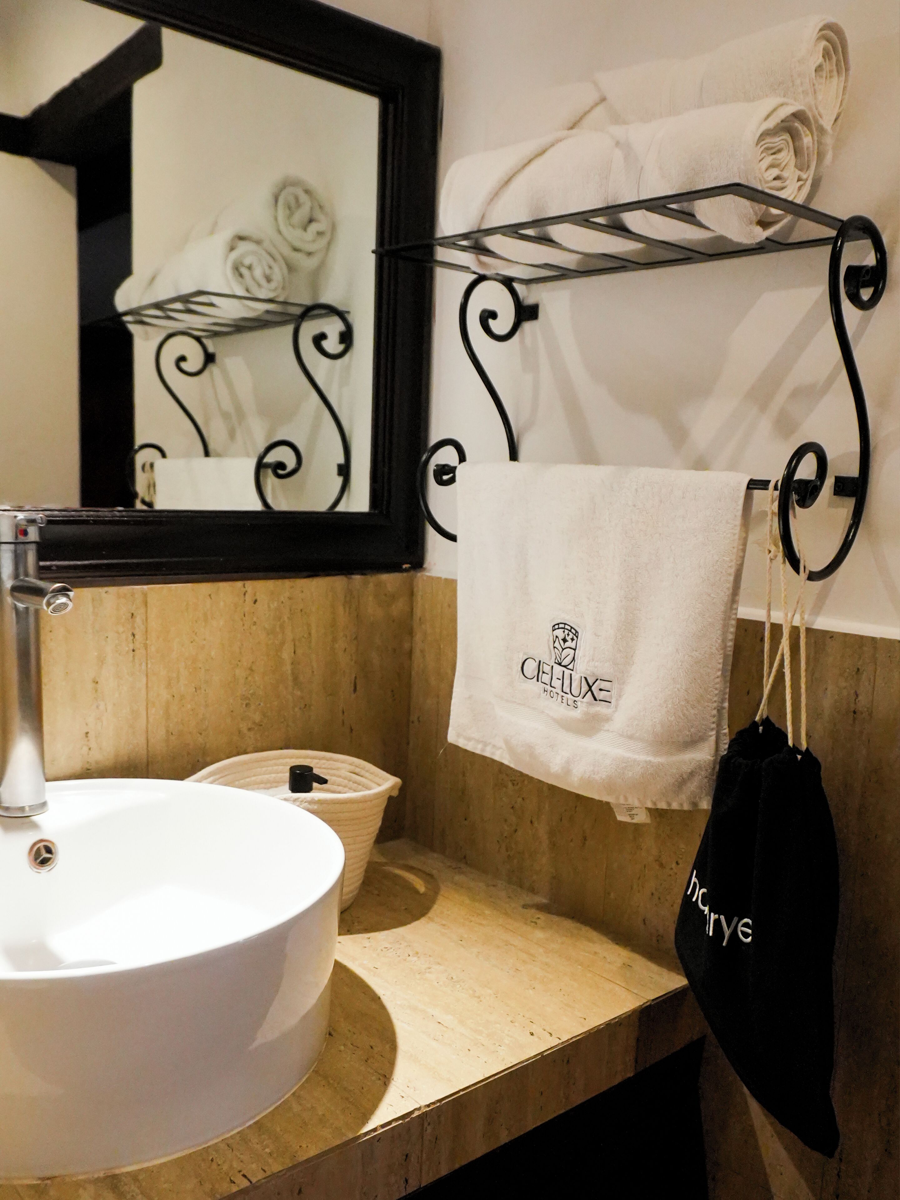 A bathroom with a white sink, a mirror, a towel rack with a towel, and a black bag hanging on the rack.