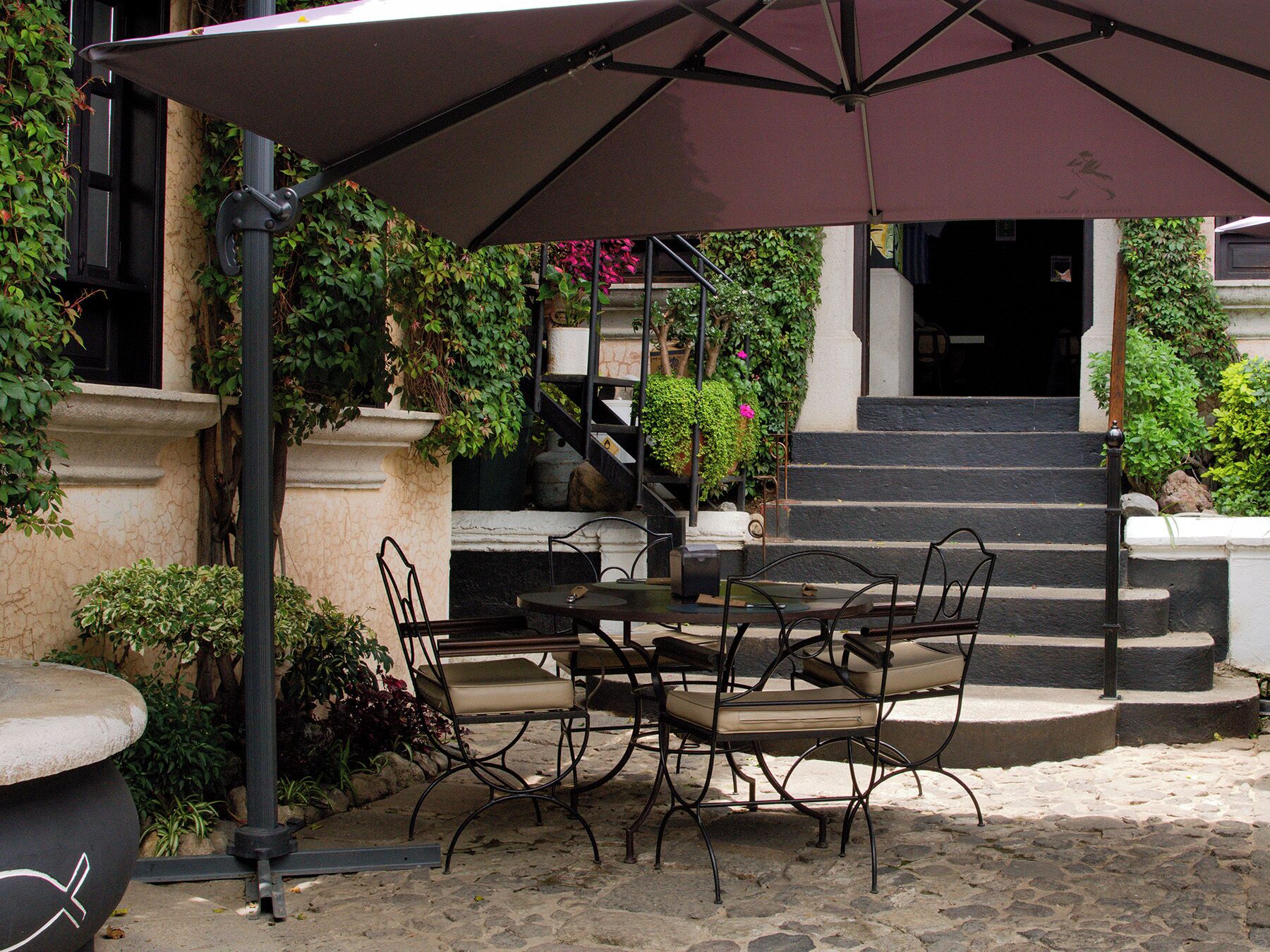 Un patio al aire libre con mesa y sillas, una zona cubierta y escalones que conducen a la entrada de un edificio.