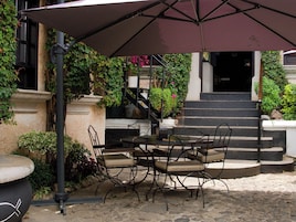 An outdoor patio with a table and chairs, a covered area, and steps leading to a building entrance.