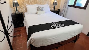 Habitación de hotel con pared de piedra, cama con ropa blanca, dos lámparas de noche y ventana con vistas.