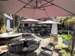 En udendørs terrasse med borde og parasoller, en springvand og en trappe, der fører op til et højere niveau.