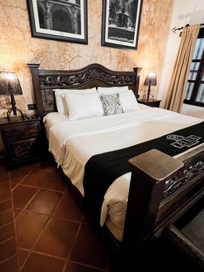 A neatly made bed with a black headboard, two bedside lamps, and a framed picture above it. - Ciel-Luxe Hotels (Antigua Guatemala)