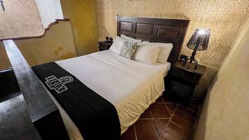 Una camera d'albergo con un letto, un comodino con una lampada, un condizionatore d'aria a parete e carta da parati fantasia.