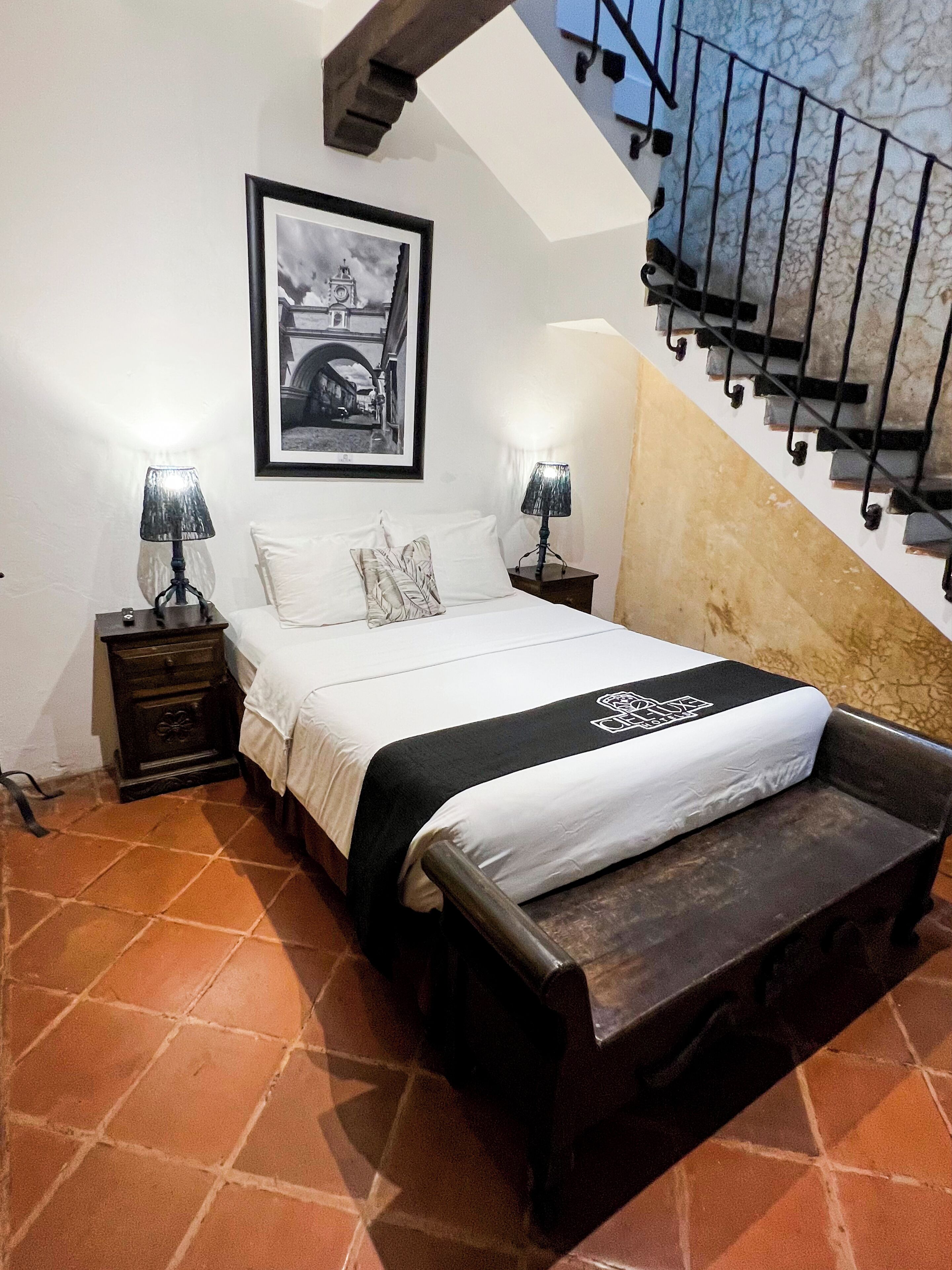 Un dormitorio con una cama, dos mesitas de noche con lámparas, un cuadro enmarcado en la pared y una escalera.