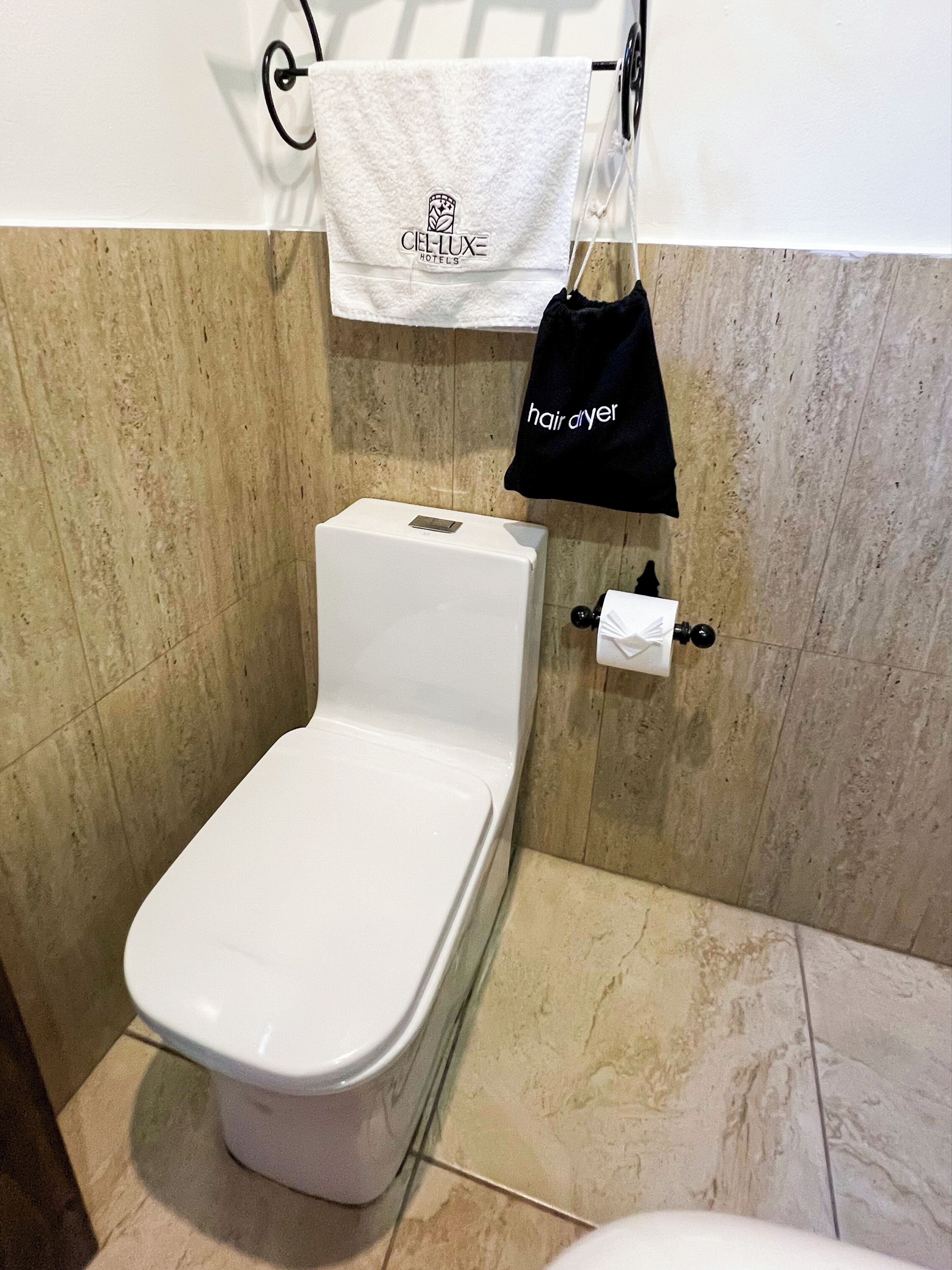 A bathroom with a white toilet, a towel rack with a towel, and a hair dryer bag.