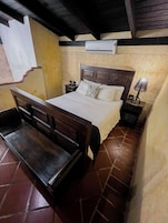 A bedroom with a wooden bed, a nightstand, a lamp, and a wall-mounted air conditioner.