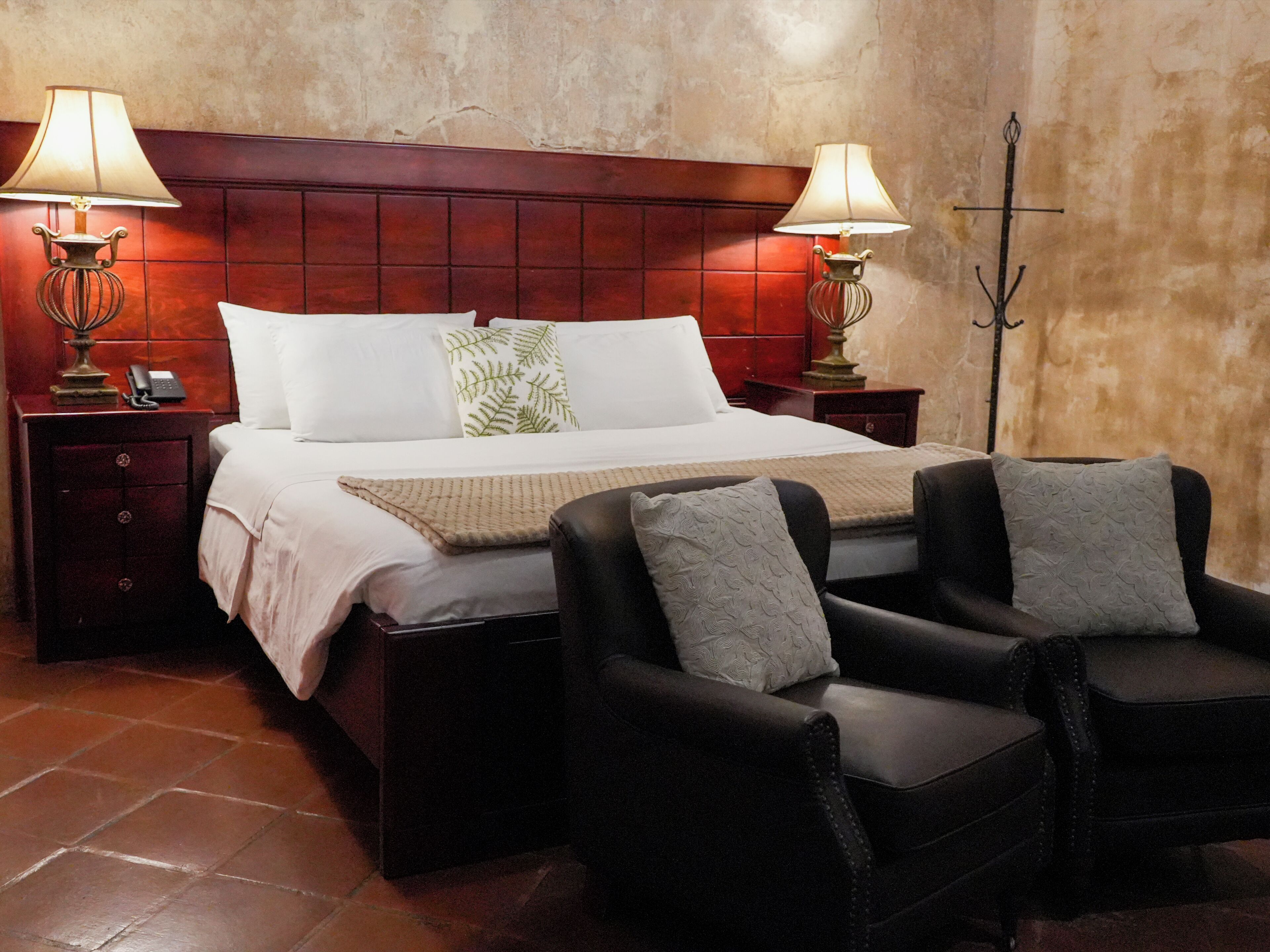 Ein Hotelzimmer mit einem großen Bett, zwei Nachttischen mit Lampen, einem Beistelltisch und zwei Sesseln.