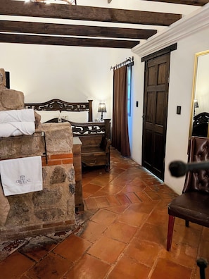Ein Hotelzimmer mit Steinwand, einem Bett mit Holz Kopfteil, einem Holzstuhl, einem Schreibtisch mit Lampe und einer Tür mit Spiegel.