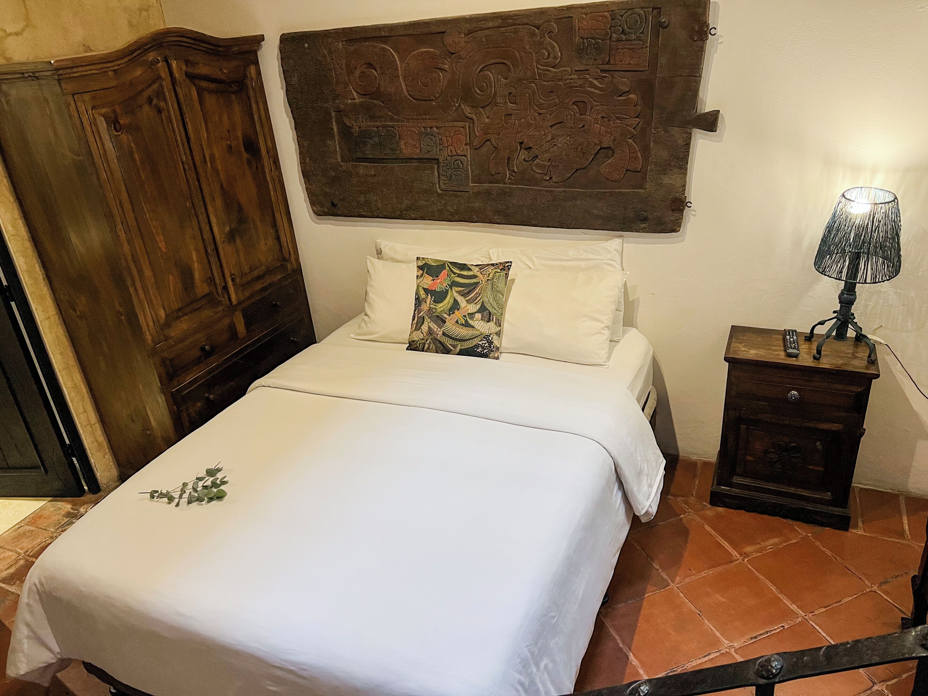 A bed with white linens, a decorative pillow, a nightstand with a lamp, and a wooden headboard.