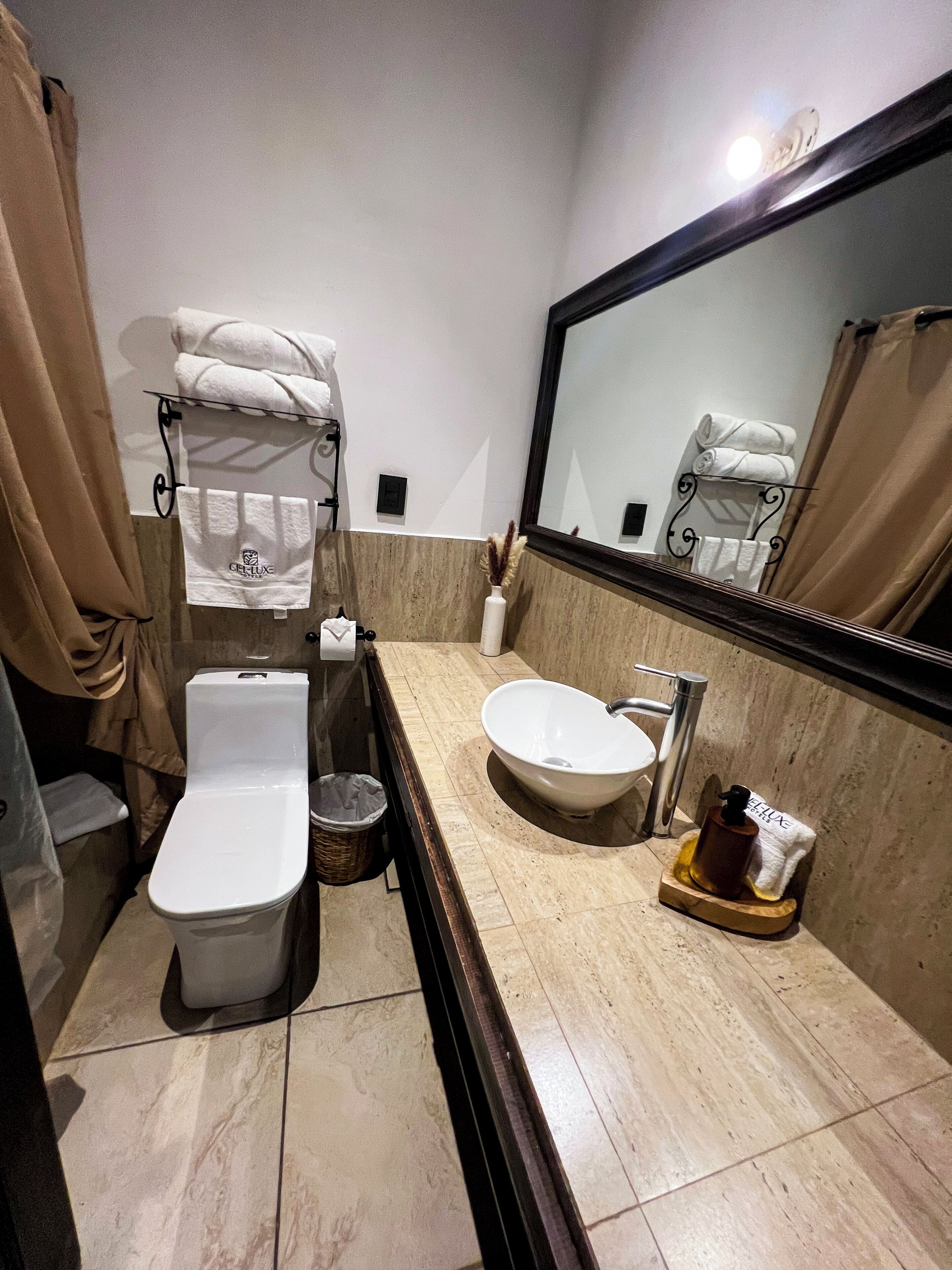 A bathroom with a toilet, sink, and mirror. There are towels and toiletries on the counter.