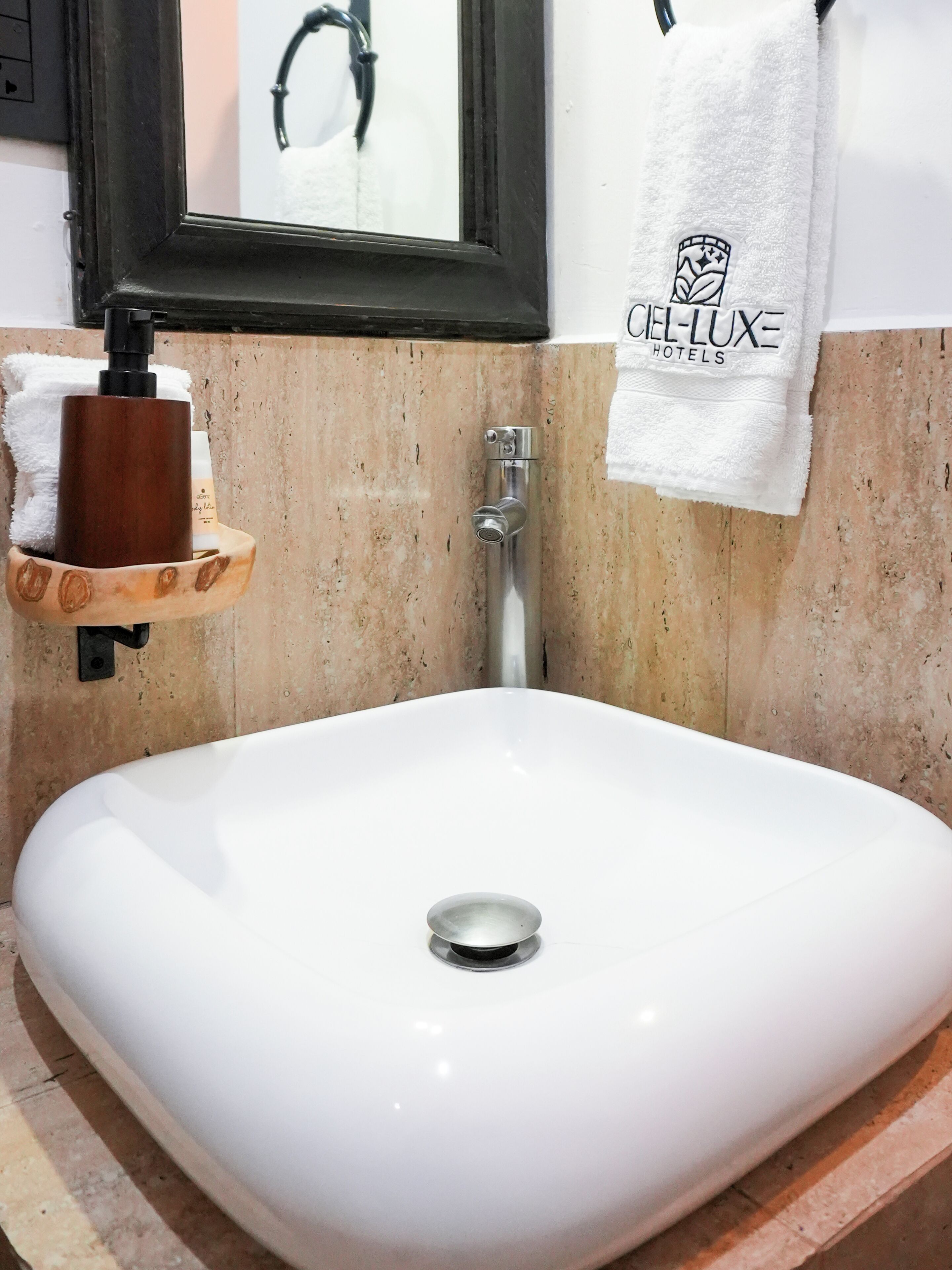 A bathroom with a white sink, a wooden soap dish, a towel rack with a hotel logo, and a mirror with a black frame.