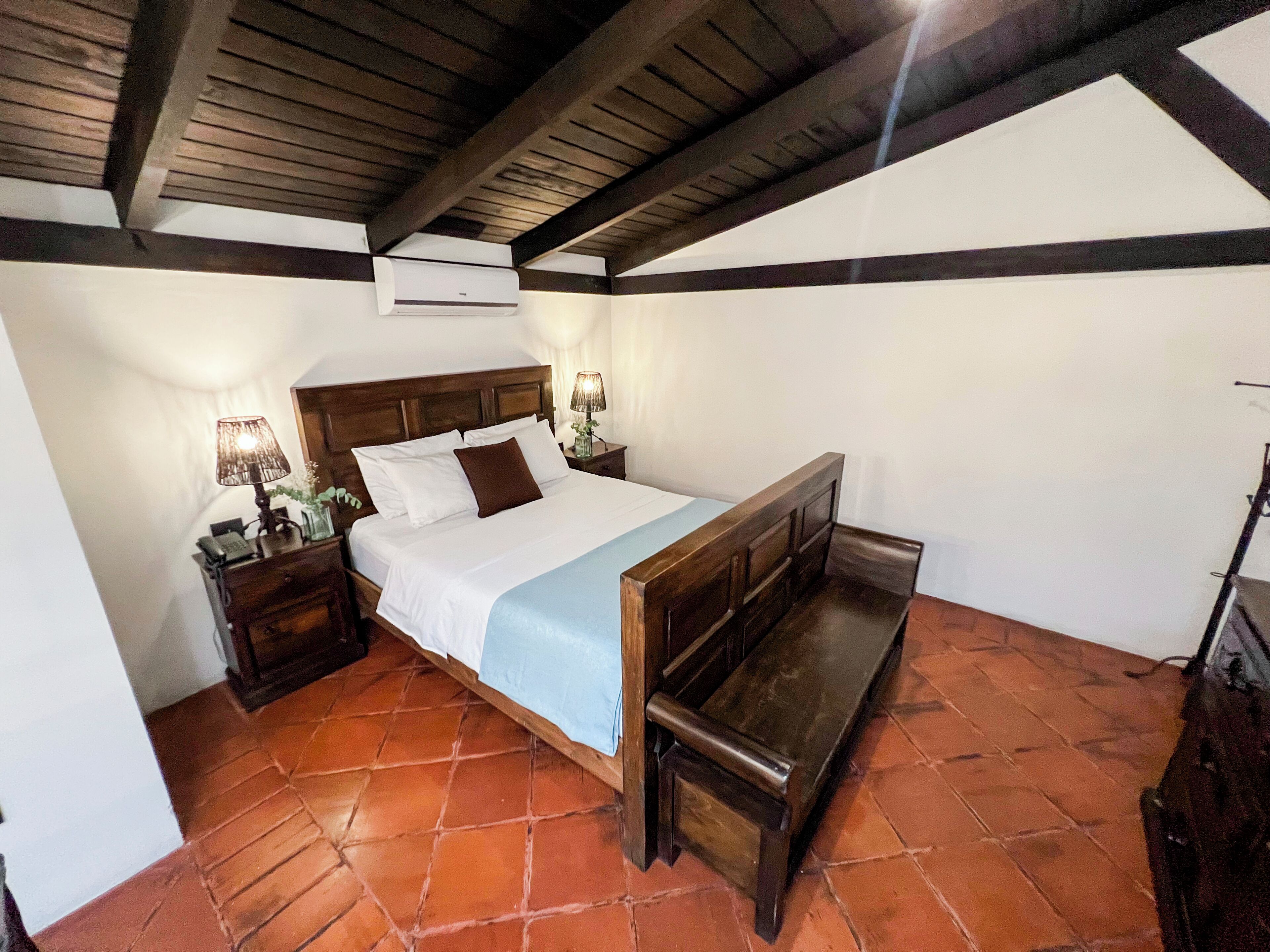 Un dormitorio con una cama de madera, una mesita de noche con lámpara y un equipo de aire acondicionado en la pared.