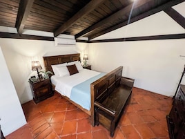 A bedroom with a wooden bed, a nightstand with a lamp, and an air conditioning unit on the wall.