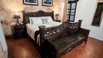 Un dormitorio con una cama de madera, dos mesitas de noche con lámparas, un banco y vista a un edificio a través de una ventana.