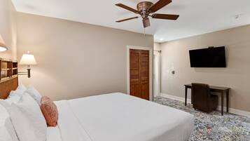 Une chambre d’hôtel avec un lit, un ventilateur de plafond, une télévision, un bureau et une moquette à motifs.