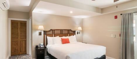 A hotel room with a bed, a nightstand, a lamp, a ceiling fan, and a door.