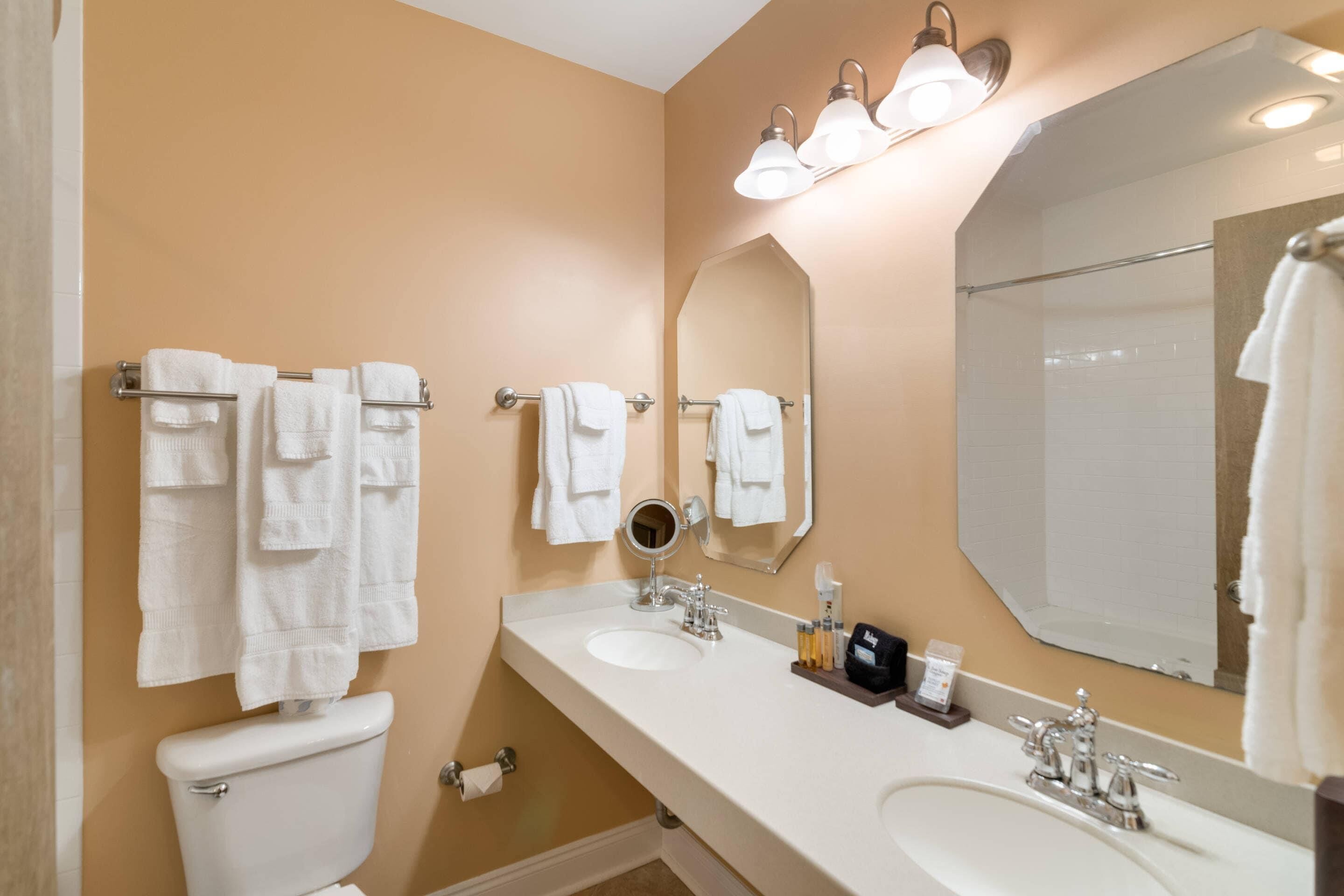 A bathroom with two sinks, a toilet, a large mirror, and multiple towels.